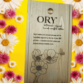 ORY wooden gift box with engraved logo and floral illustration, displayed on a vibrant yellow background framed by daisies and pink flowers, highlighting personalized botanical skincare gifting.