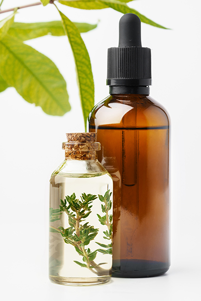 Amber dropper bottle and glass vial displaying bi-phasic botanical infusion with suspended green herbs, illustrating ORY Skincare’s dual-phase infusion of water-based hydration and oil-soluble botanical actives.