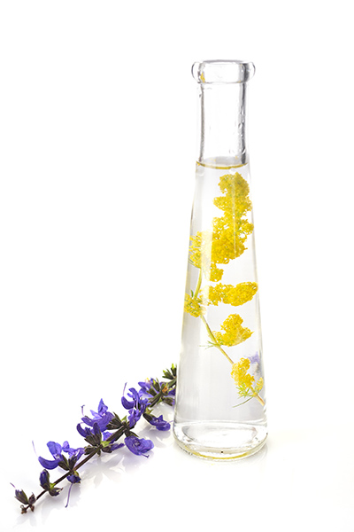 Glass vessel containing bi-phasic botanical infusion with suspended yellow blossoms, representing ORY Skincare’s dual-phase formulation that combines water-based hydration and oil-soluble botanical actives.