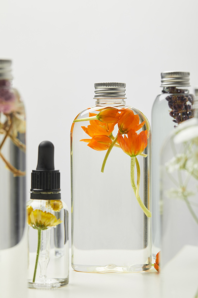 Glass bottles displaying bi-phasic botanical infusions with suspended flowers and herbs, illustrating ORY Skincare’s dual-phase infusion process combining water-based hydration and oil-soluble botanical actives.
