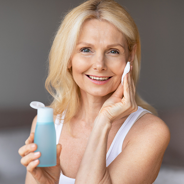 Woman using bi-phasic infusion skincare with a cotton pad, demonstrating a dual-phase oil and water formula that gently cleanses, hydrates, and soothes skin.