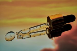 Glass dropper dispensing a bi-phasic serum with visible oil and water droplets, illustrating the synergy of oil-soluble and water-soluble skincare actives.