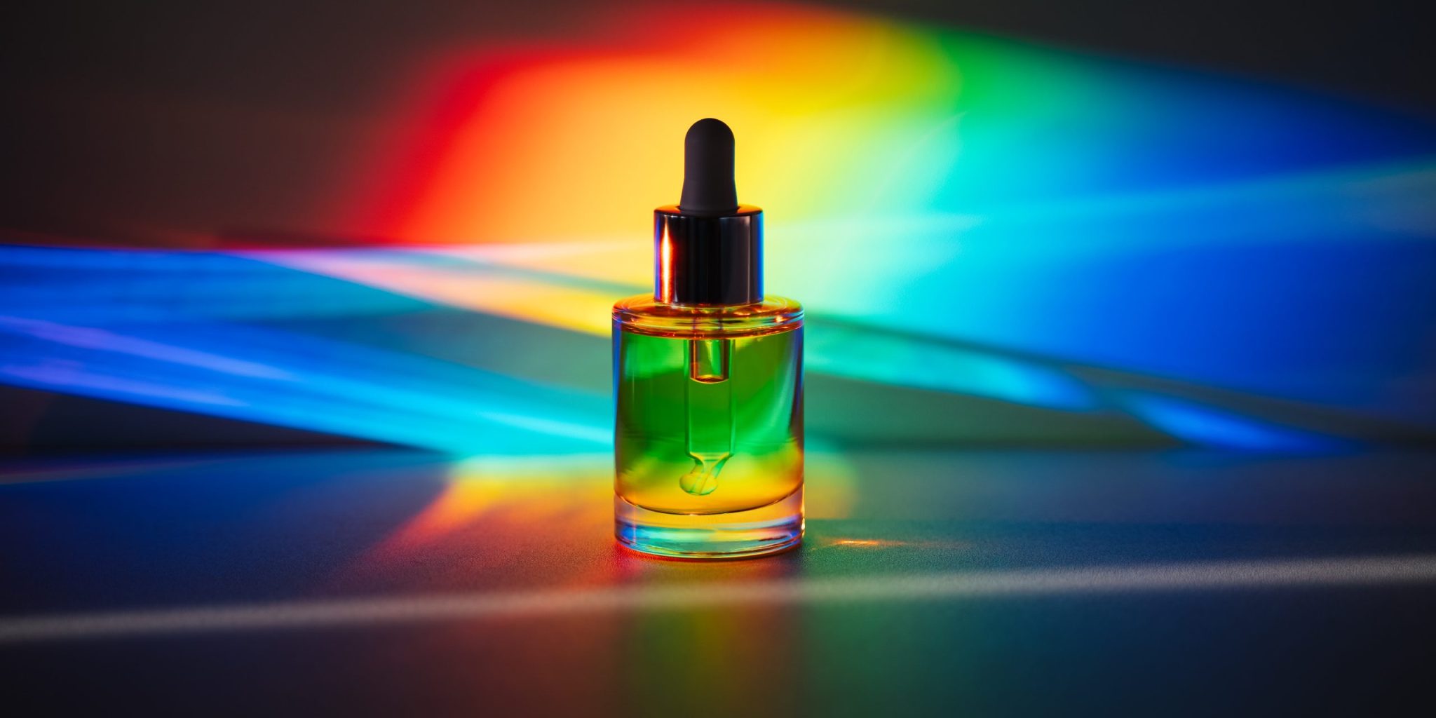 Glass serum bottle illuminated by a full color spectrum of light, symbolizing the emotional and psychological impact of color in skincare rituals.