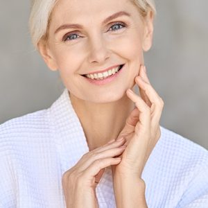 Smiling mature woman with radiant skin touching her face, representing ORY Skincare’s hydrating and firming toner for mature skin.